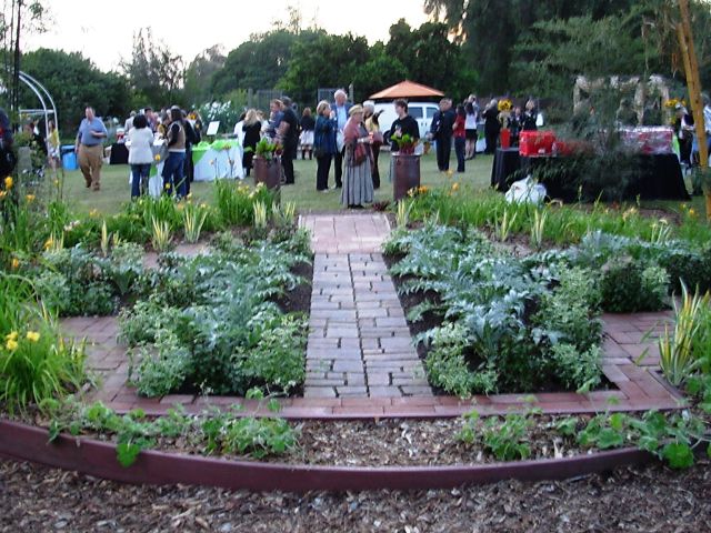 The circular garden of edibles features silvery, white-and-green variegated, and dark-leaf plants as center elements, with gold-and-green variegated plants around the perimeter