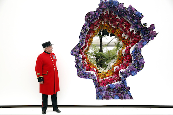 Chelsea pensioner Dewi Treharne poses with a floral tribute to Britain's Queen Elizabeth for her 90th birthday desinged by florist Veevers Carter on the New Covent Garden Flower Market stand at the RHS Chelsea Flower Show 2016 in London, UK Monday May 23, 2016. RHS / Luke MacGregor