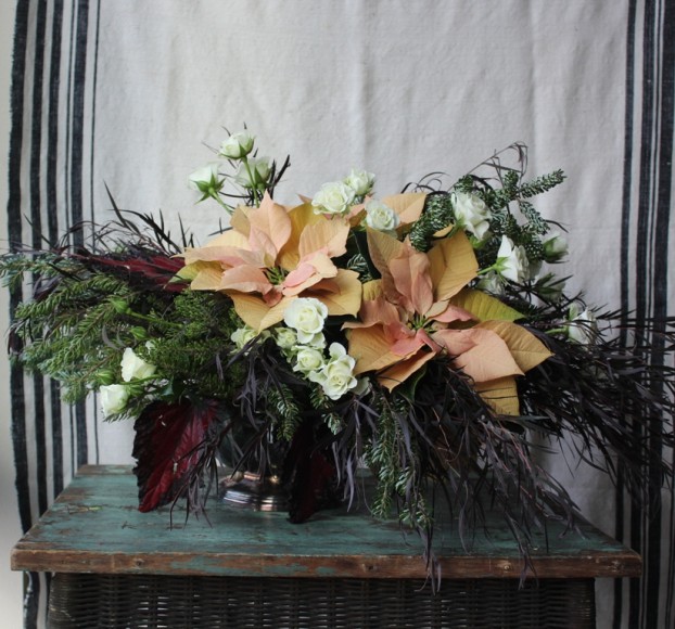 A low silver bowl, tarnished, of course, is the ideal vessel for this holiday centerpiece of poinsettias, spray roses, agonis foliage, rex begonia foliage and Korean fir